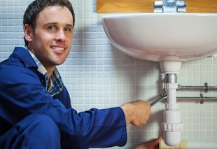 Handsome smiling plumber repairing sink in public bathroom
